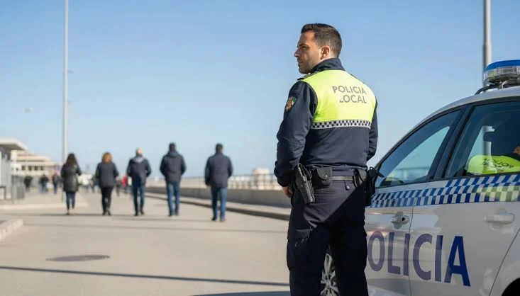 Agente de la Policía Local junto a un coche patrulla